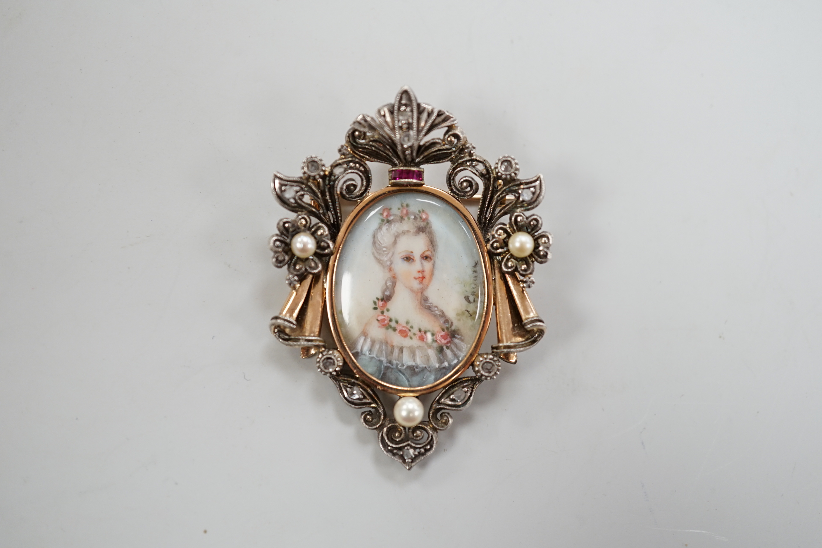 A late 19th/early 20th century continental yellow metal, seed pearl, ruby and diamond mounted pendant brooch, with inset oval miniature watercolour of a lady, indistinctly signed, 47mm, gross weight 10 grams., CITES Subm